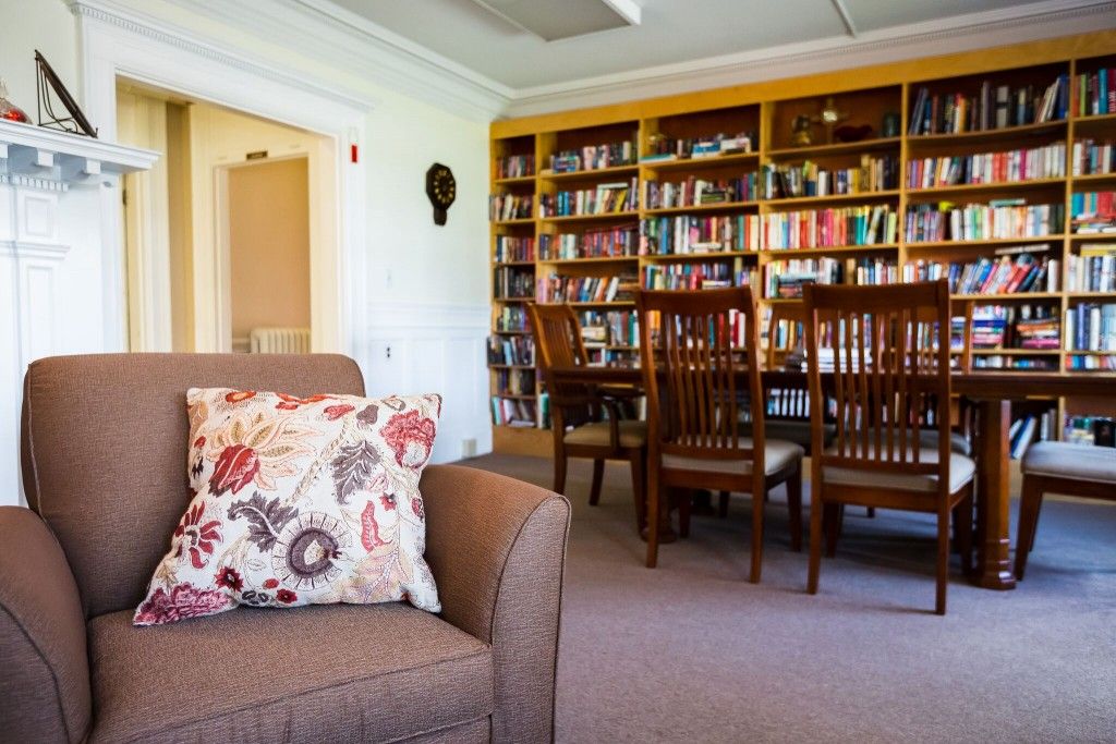 A cozy library space featuring bookshelves, a comfortable couch with floral cushions, and a wooden table set with chairs.