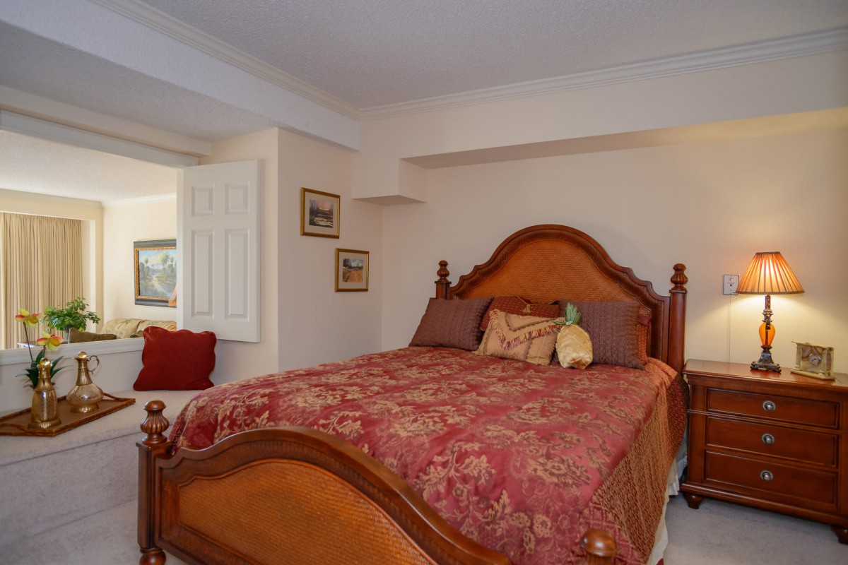 A cozy bedroom with a wooden bed frame and a red patterned comforter.