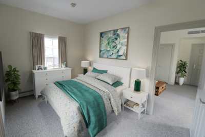 A modern bedroom featuring a bed with green accent blankets and pillows, complemented by artwork on the wall and light-colored furniture.