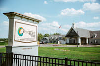A building with a sign and a fence in front, set against a backdrop of grass and a partly cloudy sky.