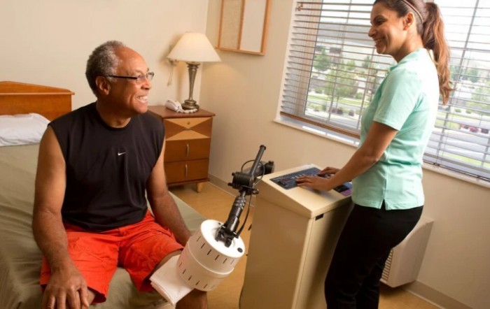 A patient sitting with a physical therapist during a rehabilitation session involving medical equipment.