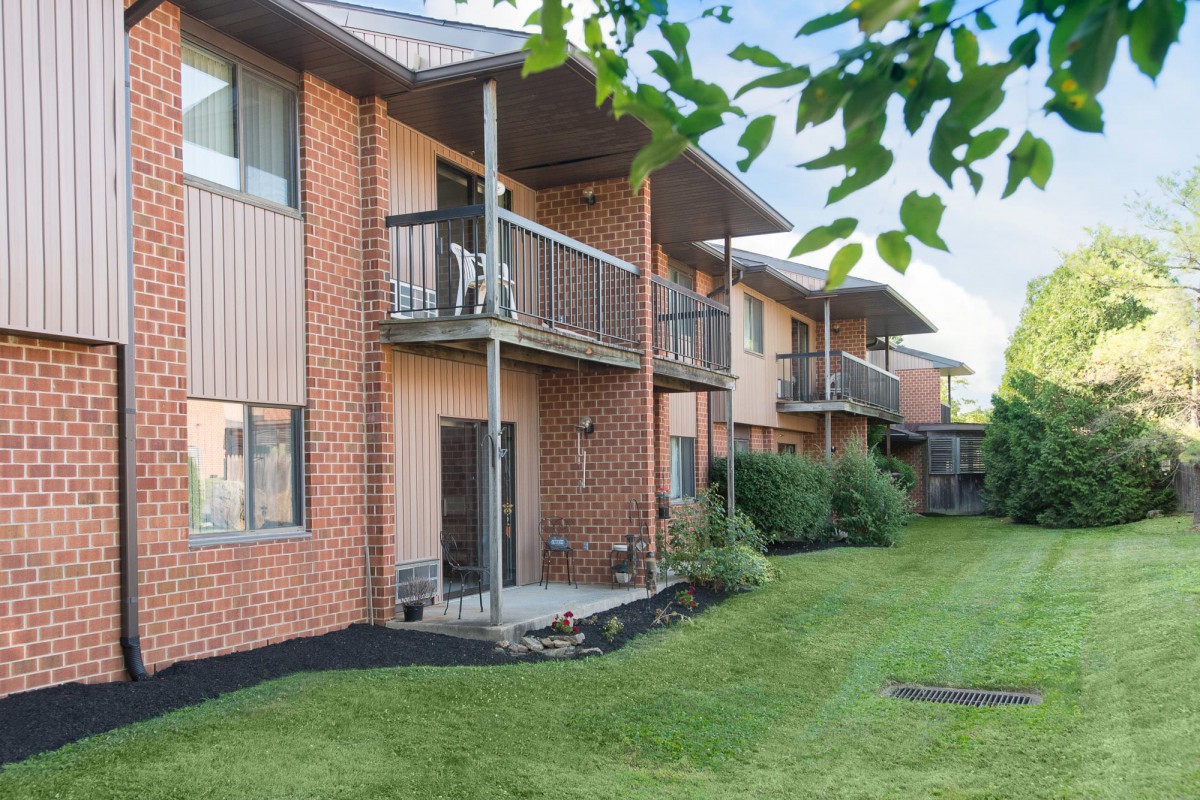 A row of brick apartment buildings with balconies and a well-maintained lawn.