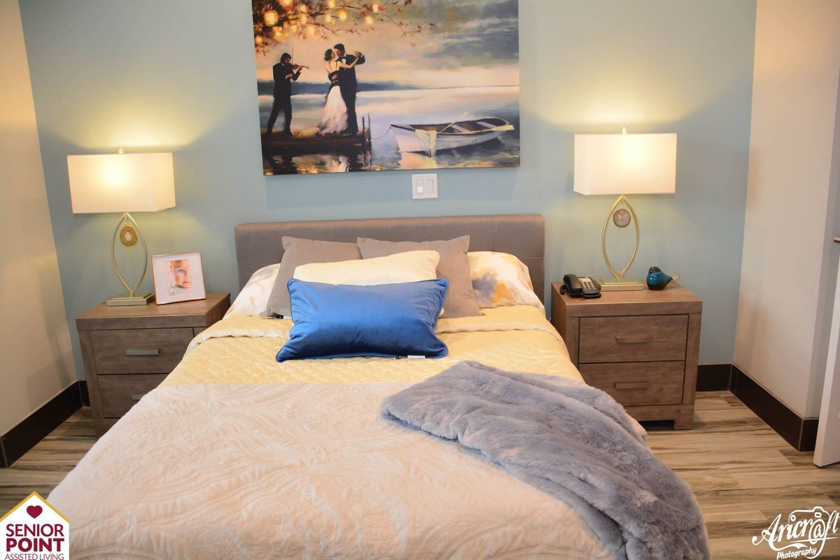 A cozy and modern bedroom with a neatly made bed, stylish artwork above the headboard, and warm lighting from two matching lamps on either side.