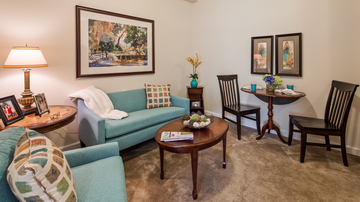 A cozy living room with a teal sofa, wooden coffee table, and decorative artwork on the walls.