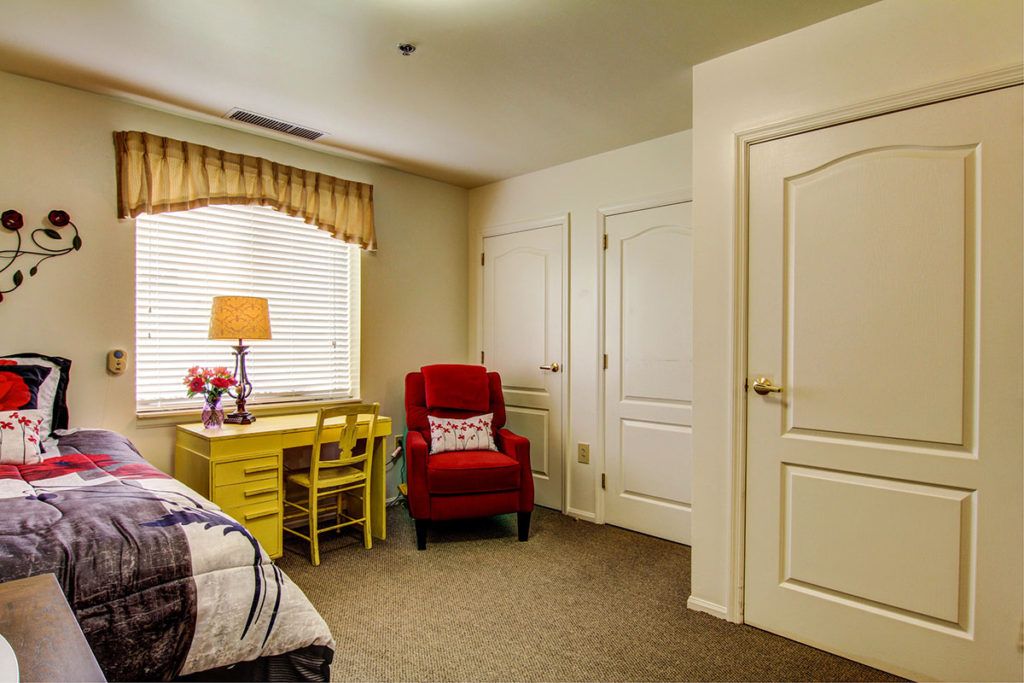 Cozy bedroom interior with a red chair and yellow desk by the window.