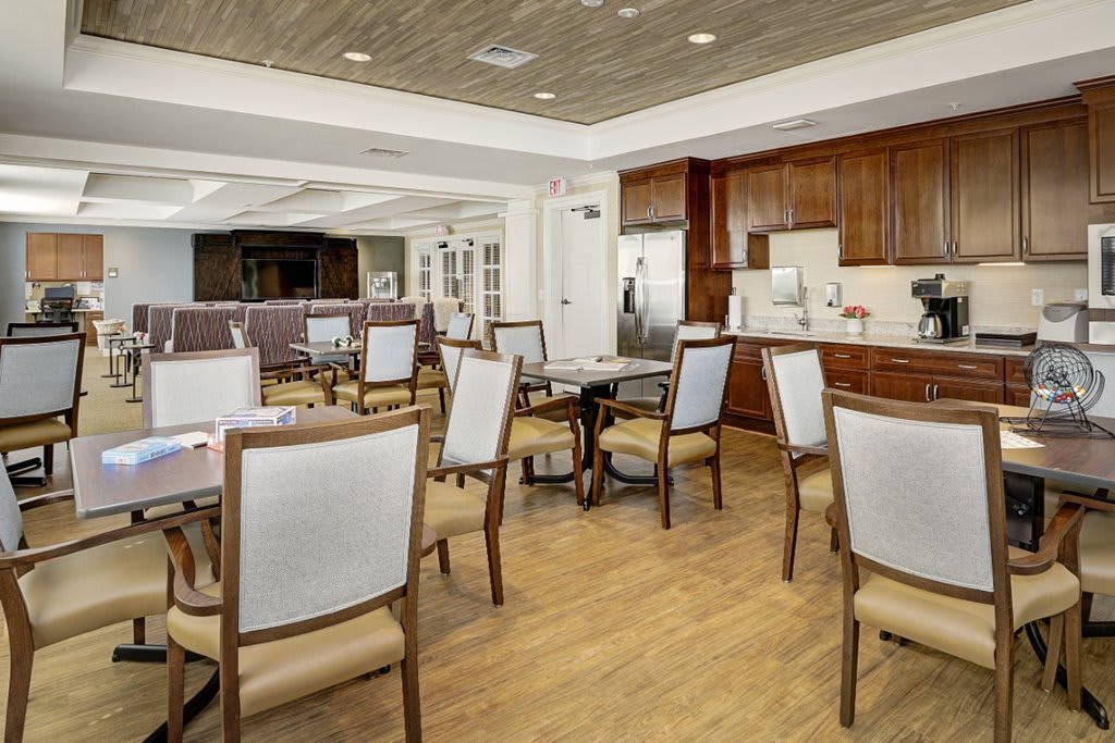 A modern dining area with several tables and chairs, featuring a hardwood floor and an adjoining kitchen space.