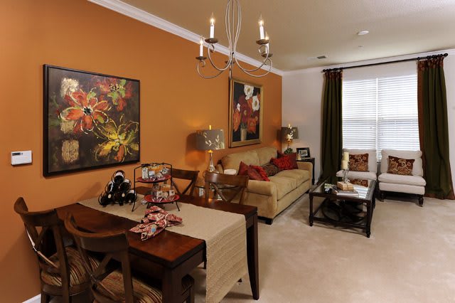 A cozy living room with an orange accent wall, featuring a dining area and colorful artwork.