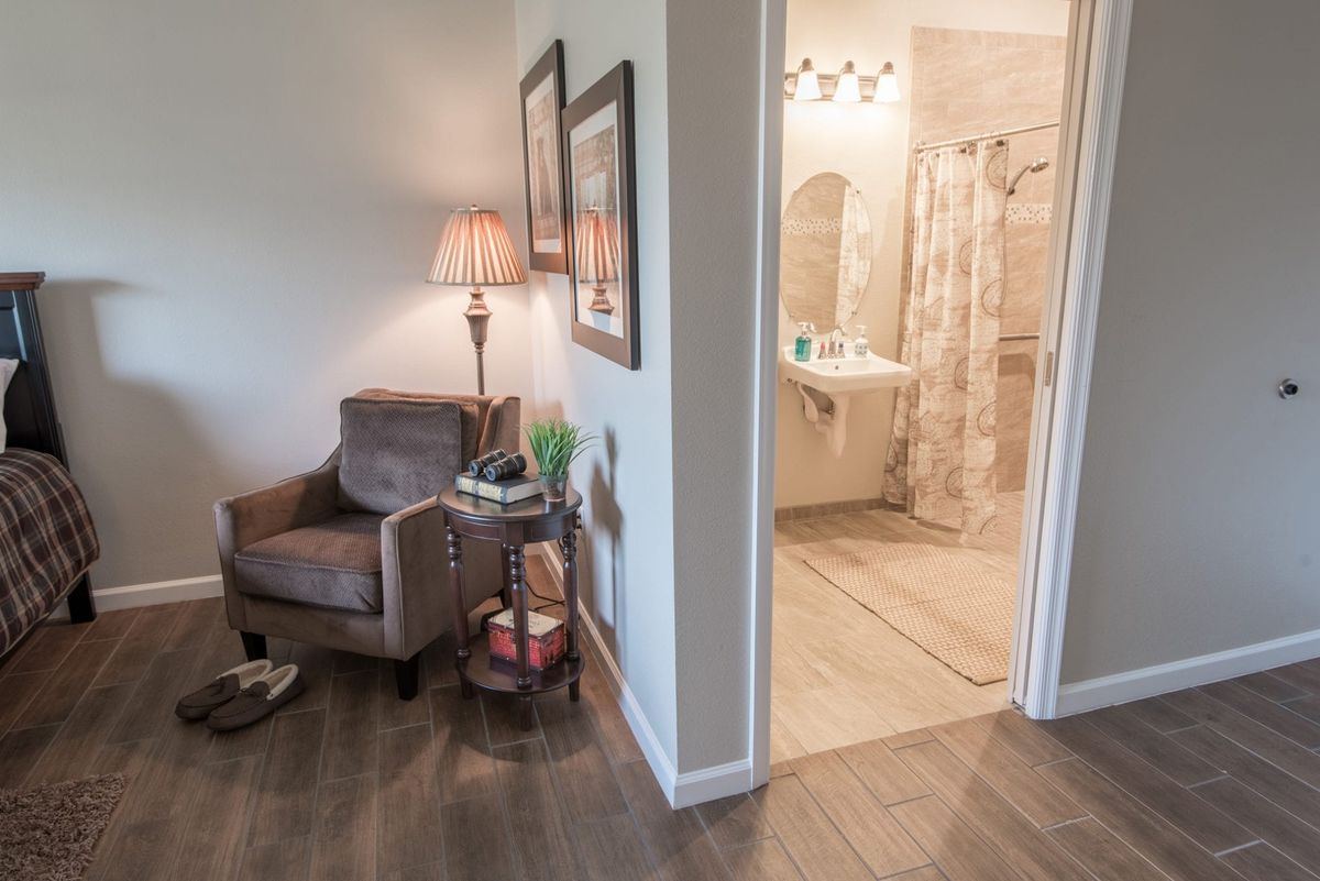 A cozy living area with a view into the bathroom, featuring an armchair and lamp.