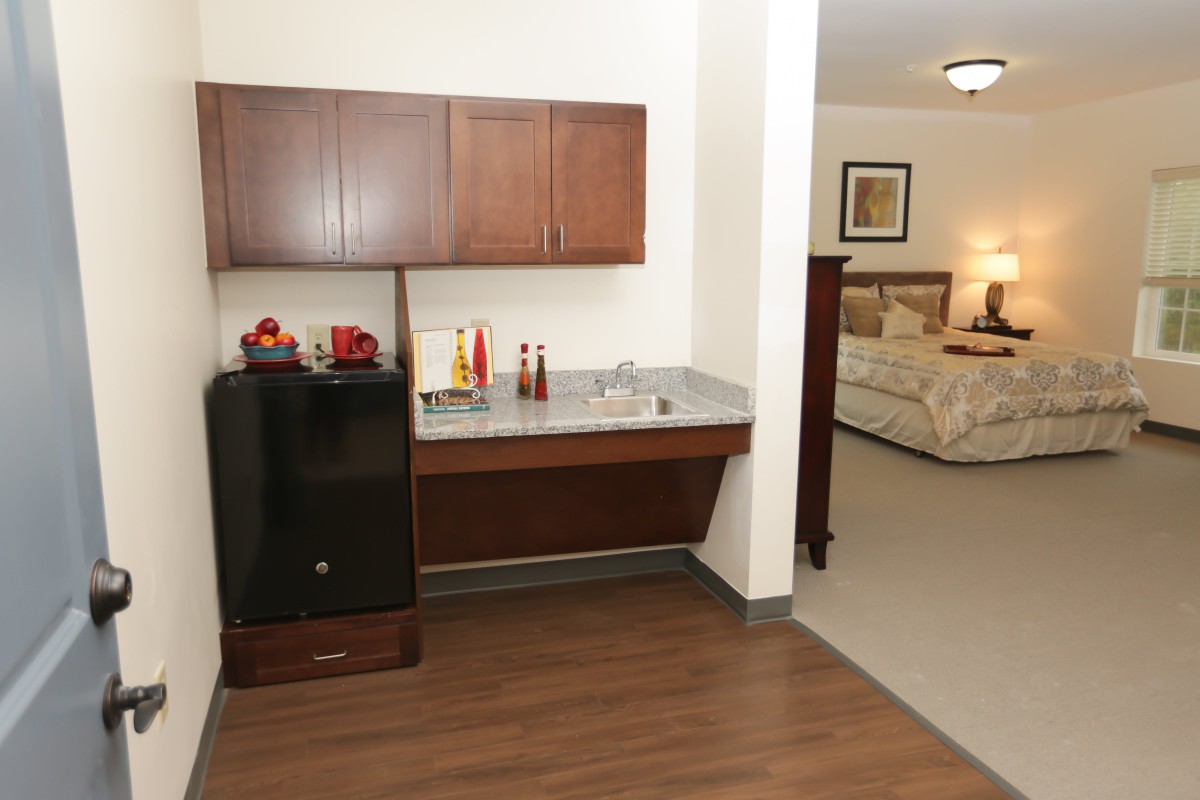 A view of a hotel room featuring a mini fridge, cabinets, and a cozy sleeping area.