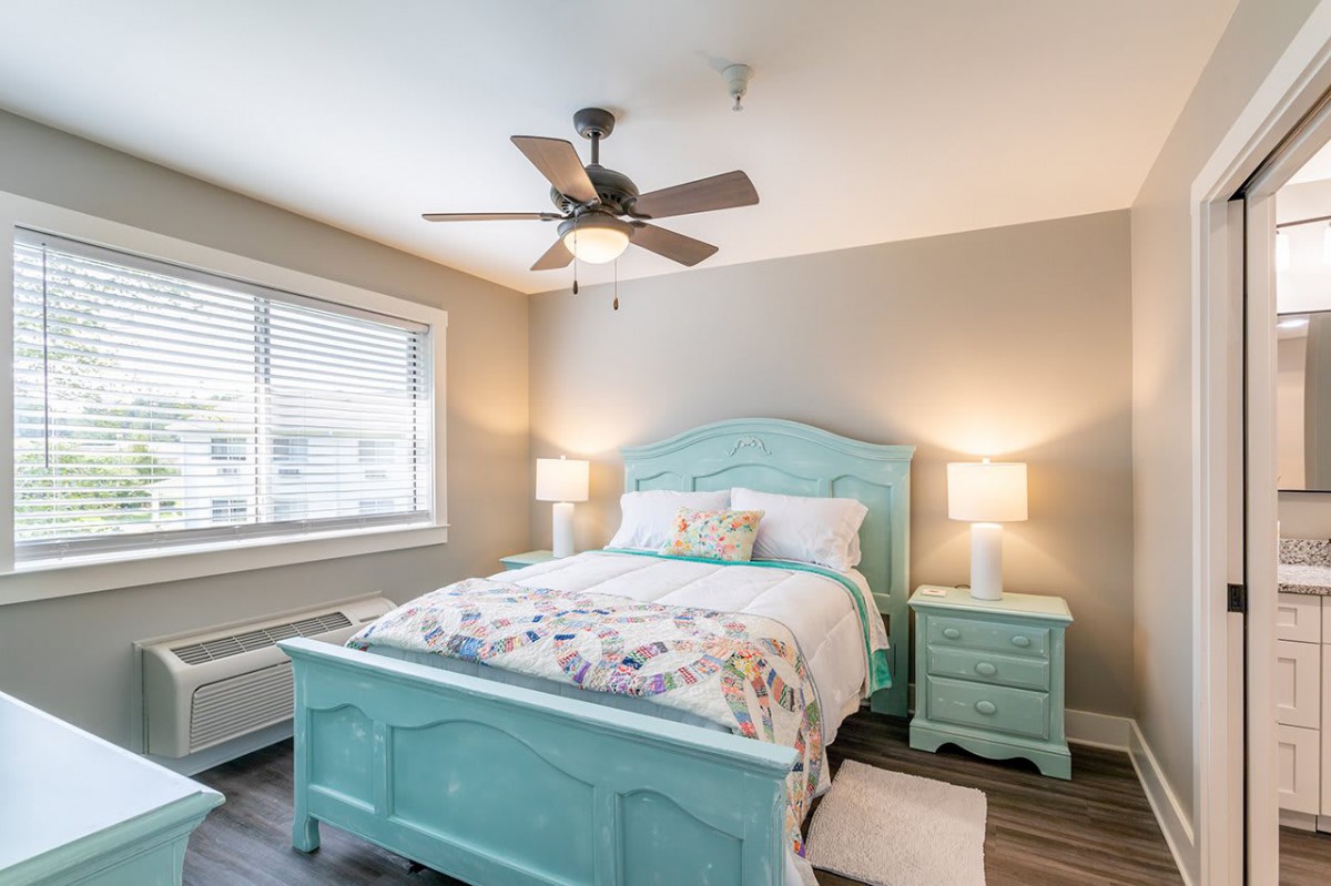 A cozy bedroom with a turquoise bed frame, matching nightstands, and a ceiling fan.