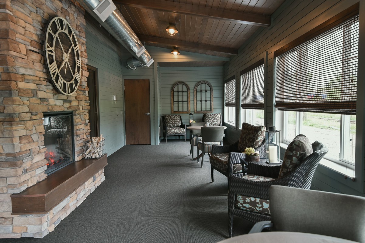 A cozy indoor seating area featuring a brick fireplace and large decorative clock, with comfortable furniture and ample windows.