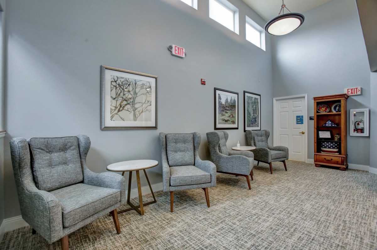 A modern waiting area with gray chairs, decorative artwork on the walls, and a carpeted floor.