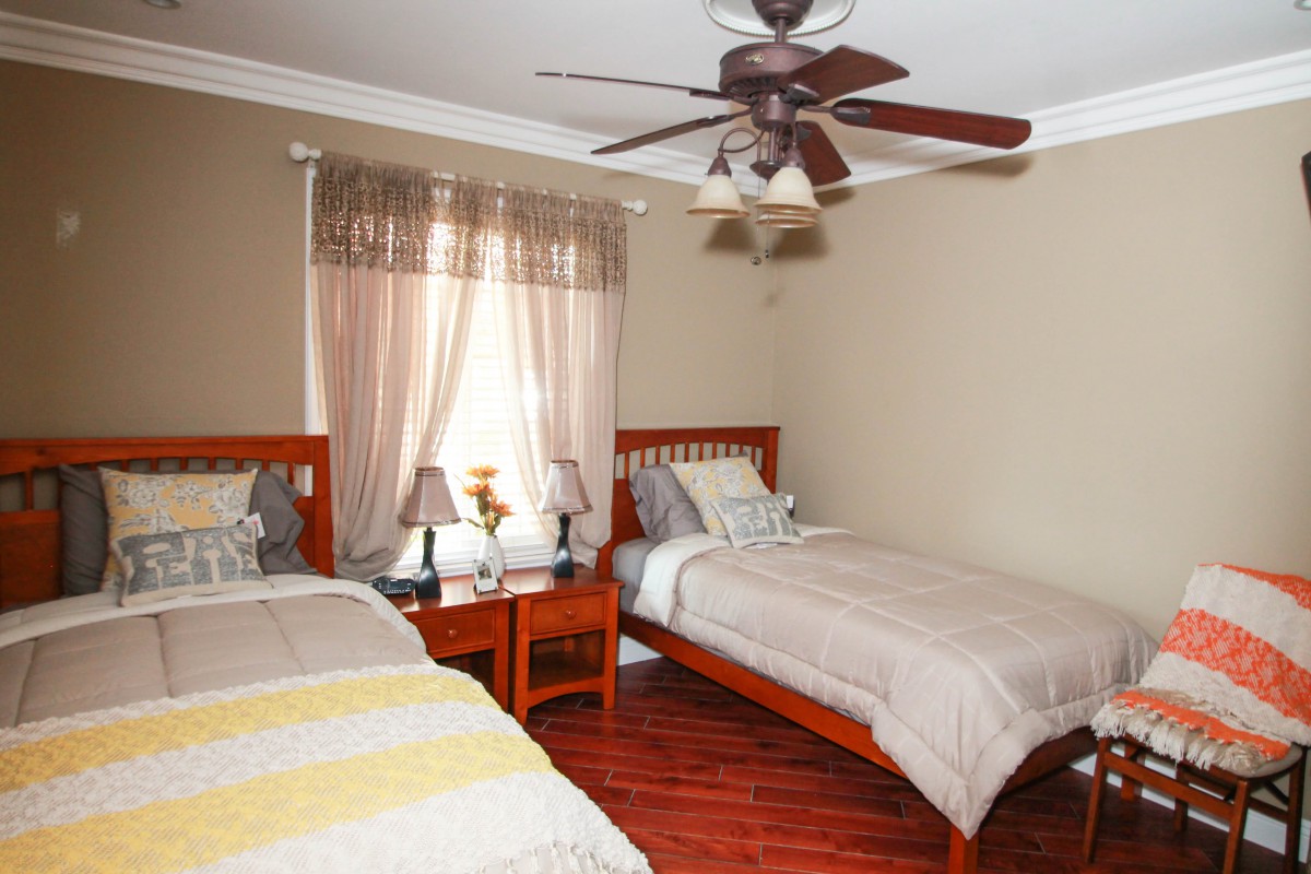 A cozy bedroom with twin beds, featuring wooden furniture and a ceiling fan.
