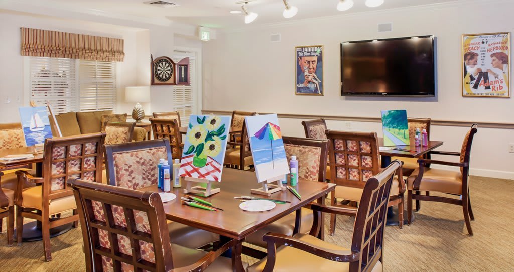 An art room with paintings on easels, surrounded by tables and chairs.