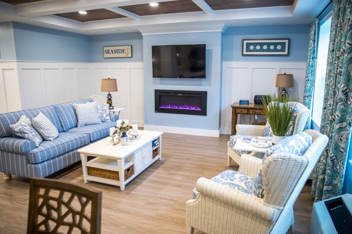 A cozy living room with blue walls, featuring a striped sofa, television, and modern fireplace.