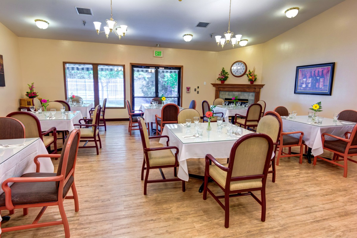 A cozy dining room with elegantly set tables and comfortable chairs, featuring a warm fireplace.