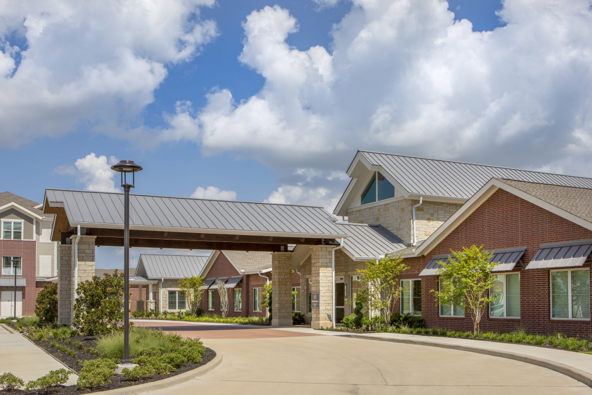 A modern building with a covered entrance and landscaped surroundings under a cloudy sky.