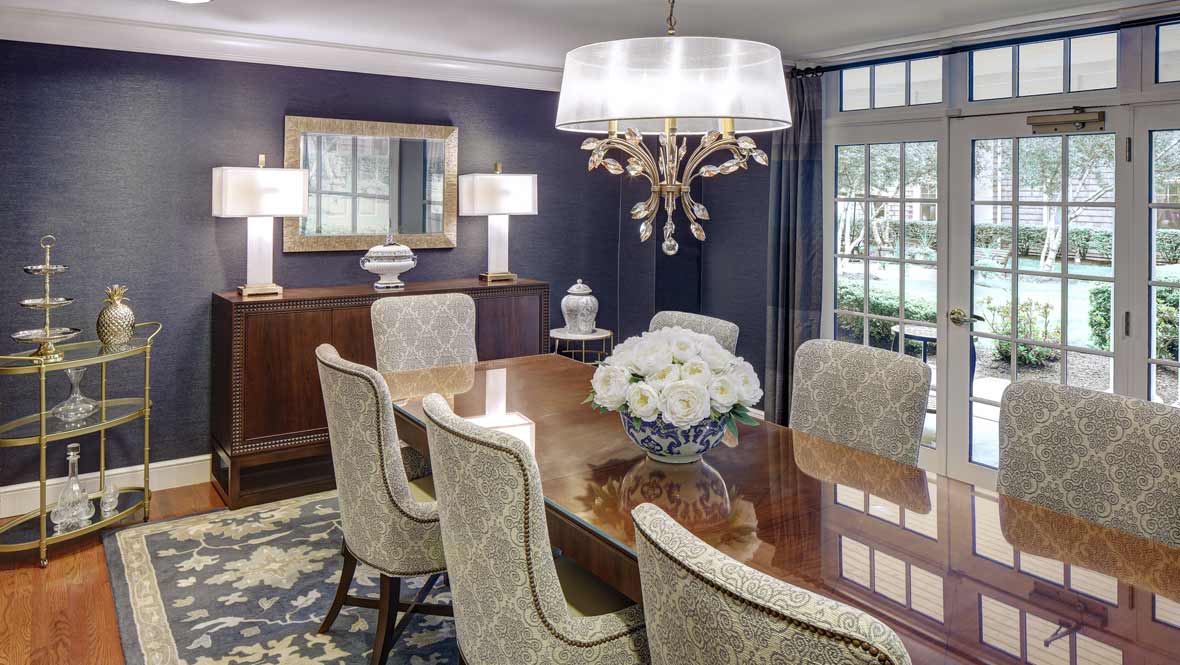 Elegant dining room with a polished wooden table and upholstered chairs, illuminated by a chandelier.