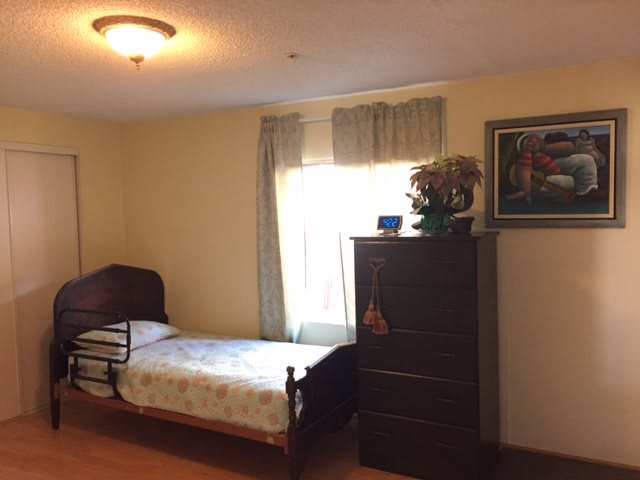 A simple bedroom with a single bed, a dresser, and a window with curtains.
