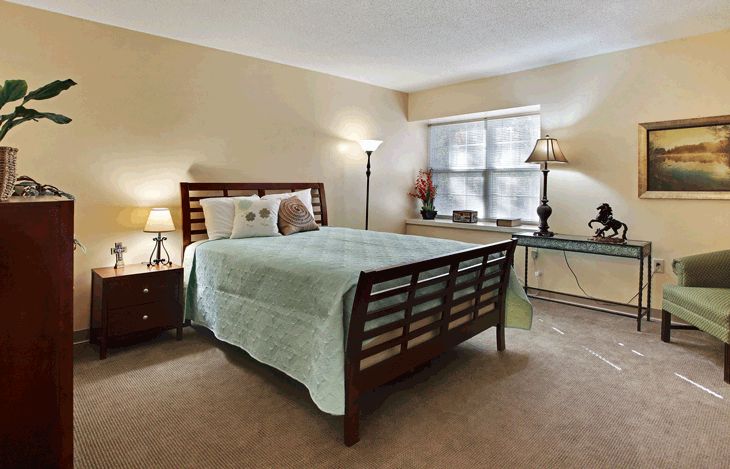 A cozy bedroom with a neatly made bed, two lamps, and a window providing natural light.