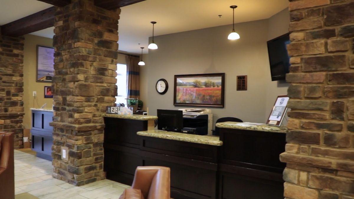 A well-lit reception area featuring a desk with a computer, decorative lighting, and a wall adorned with art.