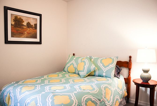 A cozy bedroom with a neatly made bed featuring patterned bedding and a framed picture on the wall.