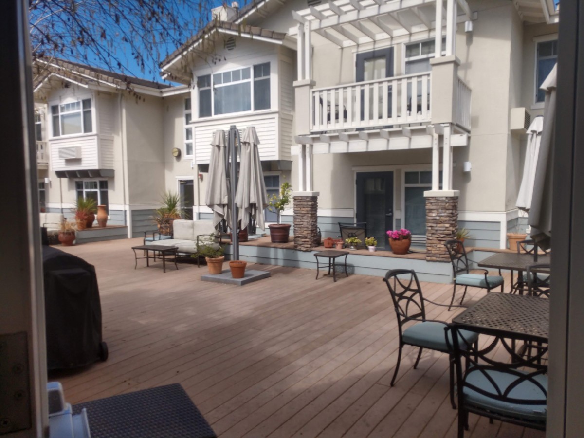 A well-furnished patio area with outdoor seating and tables, located in an apartment complex on a sunny day.
