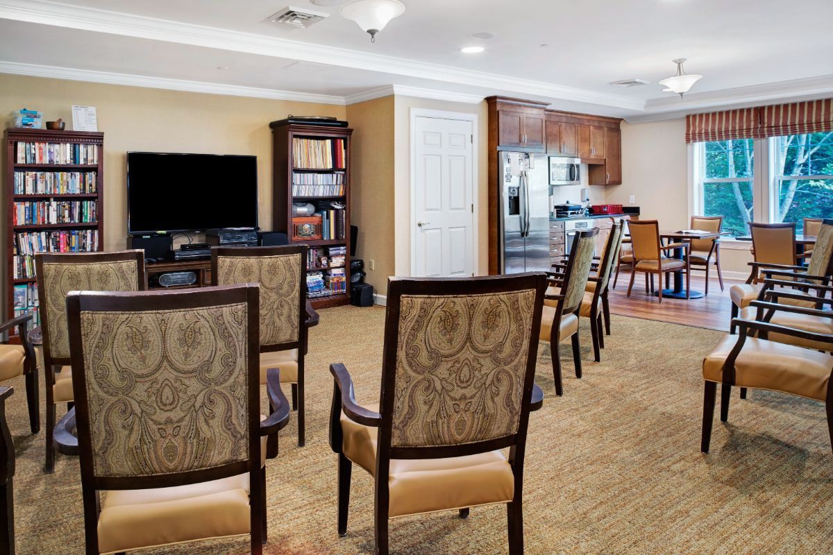 A cozy seating area with chairs facing a television and bookshelf, adjacent to a kitchenette.