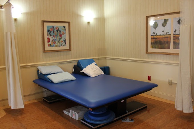 A therapy room with a blue physical therapy bed and framed artwork on the walls.