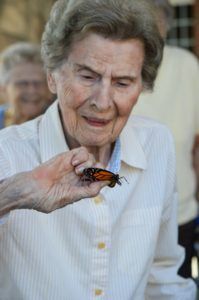 An elderly woman holding a butterfly outdoors.