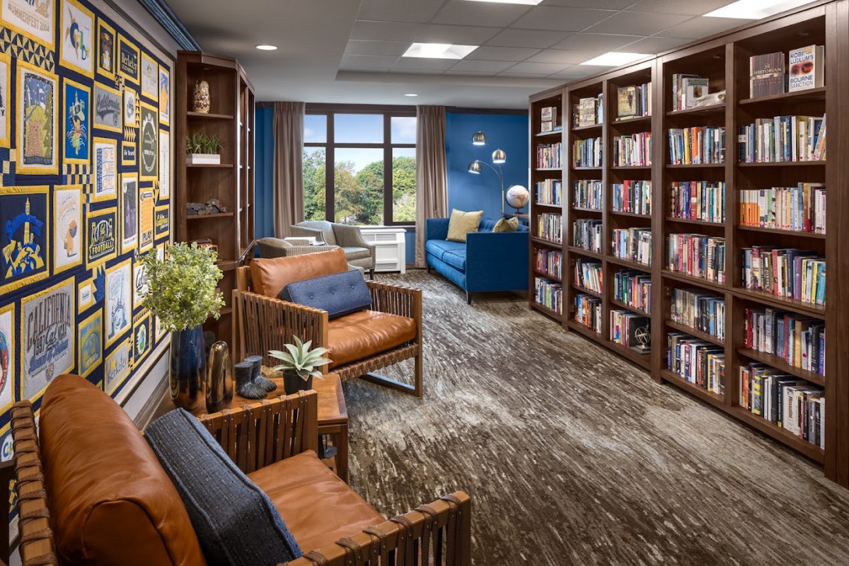 A cozy library space with bookshelves, comfortable seating, and a large window providing natural light.