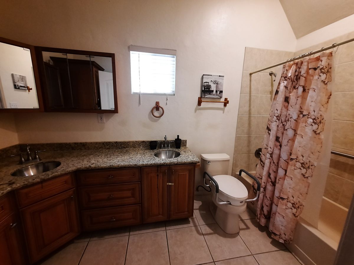A bathroom featuring a sink with a mirror, toilet, and a shower with a floral curtain.