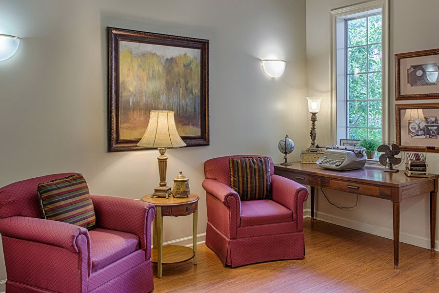 A cozy living room area with two red armchairs, a lamp, and artwork on the wall.