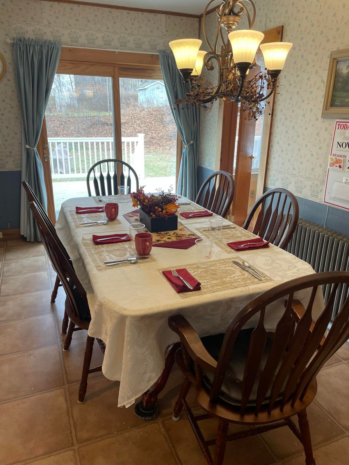A dining room table set for a meal, featuring six chairs and neatly arranged place settings under a chandelier.