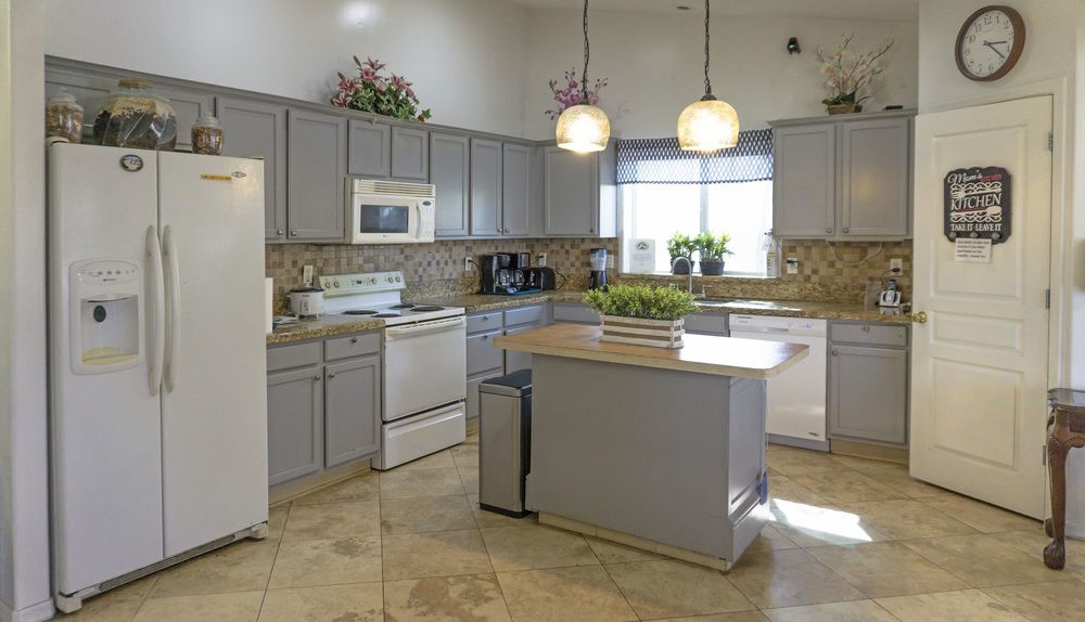 A modern kitchen with gray cabinets and a central island, featuring pendant lights and tiled flooring.