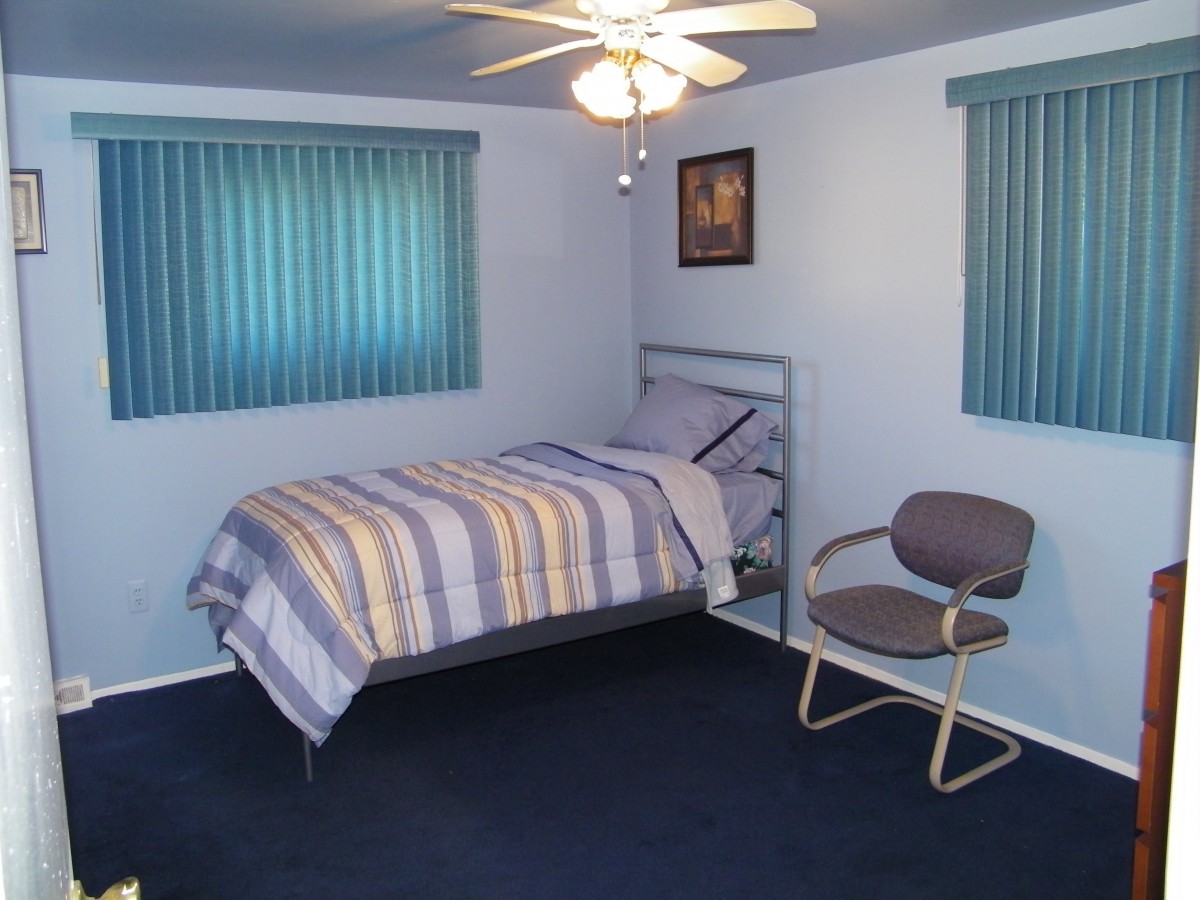 A simple bedroom with a single bed, ceiling fan, and chair.