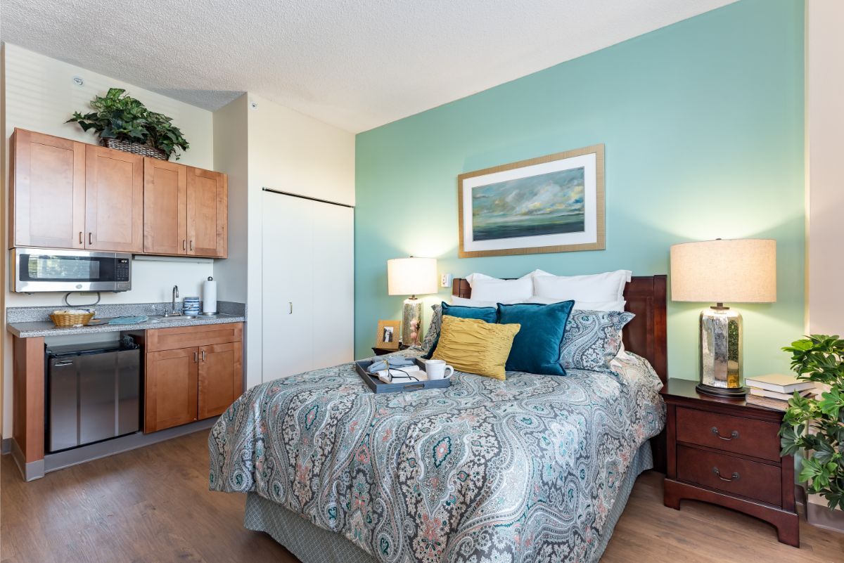 A cozy bedroom with a neatly made bed, decorative cushions, bedside lamps, and a painting hanging above the headboard.