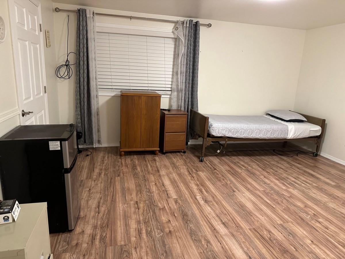 A minimalist room with wooden flooring, featuring a single bed, a small dresser, and a chest of drawers.