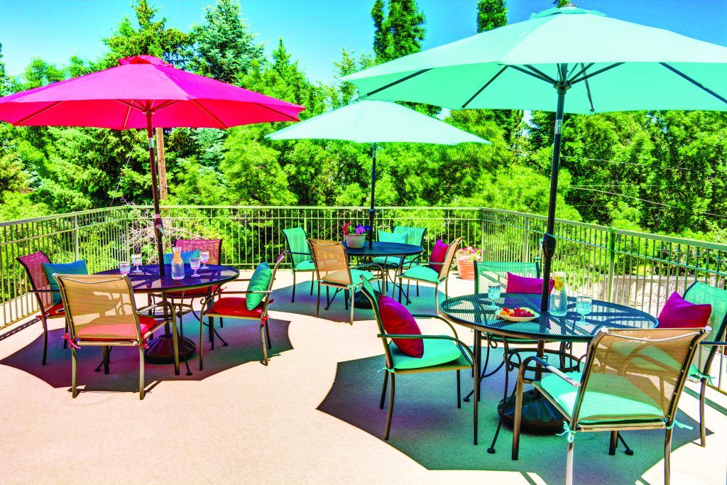 A vibrant outdoor patio with colorful umbrellas and seating, set against a lush natural background.