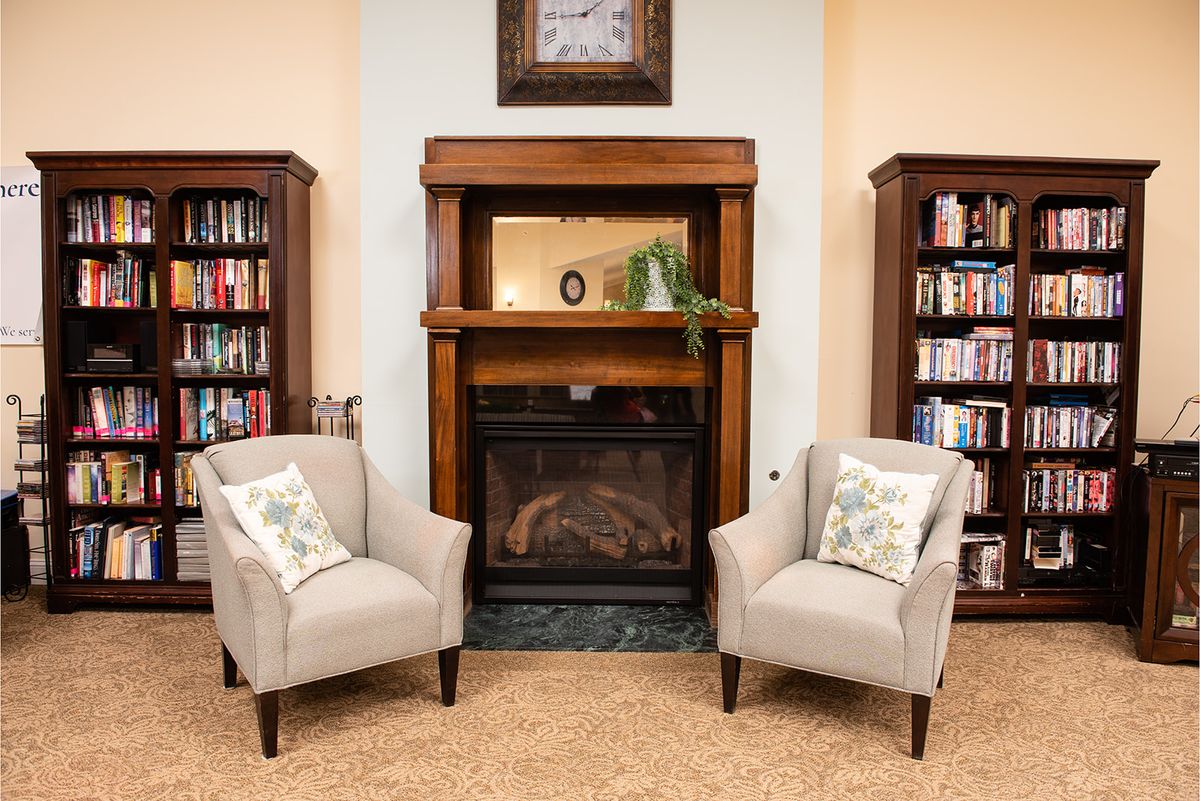 A cozy living room with armchairs and a fireplace, flanked by bookshelves.