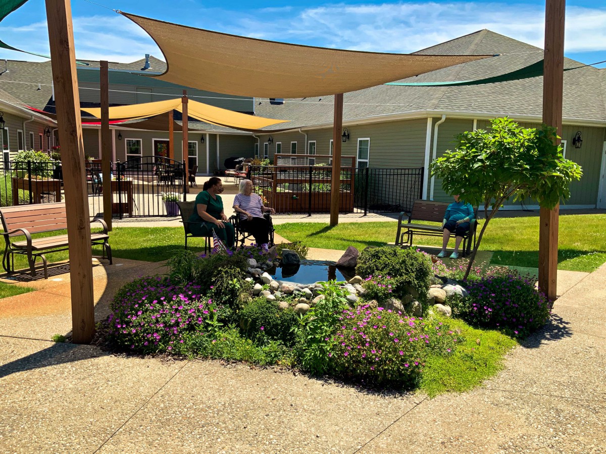 A peaceful garden setting with a shaded seating area and vibrant greenery.