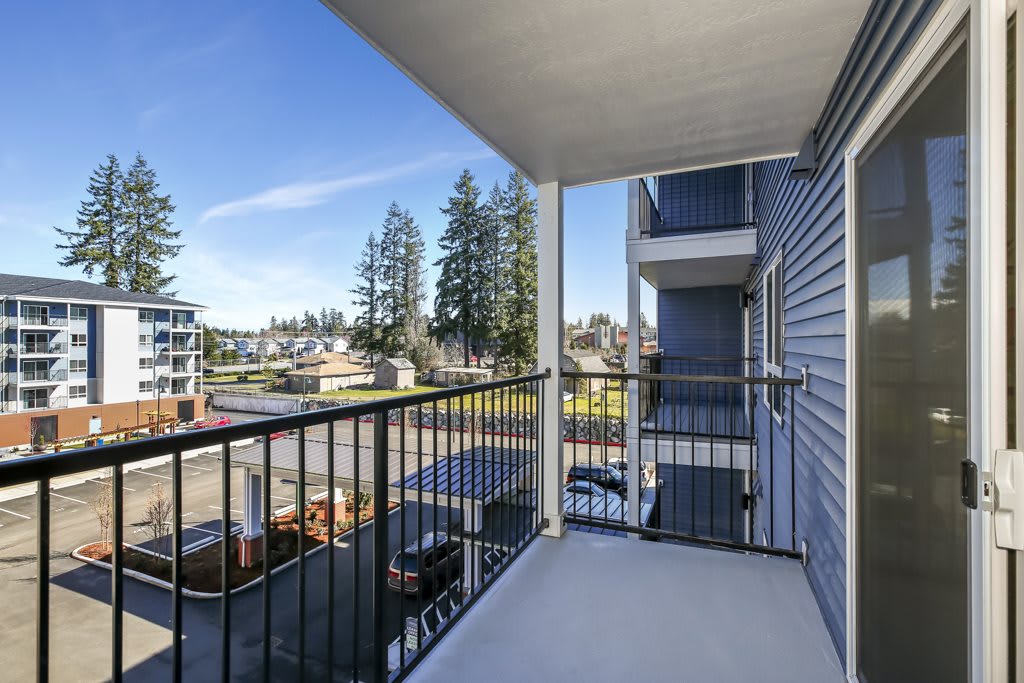 A spacious balcony with a view of neighboring buildings and tall trees under a clear blue sky.
