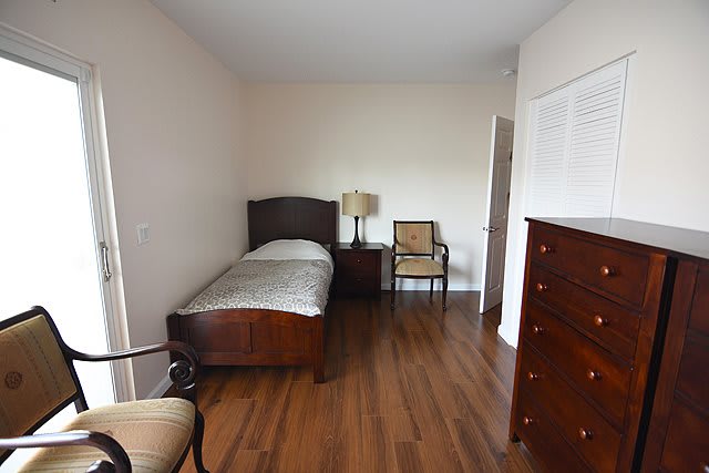 A minimalist bedroom featuring a single bed with wooden furniture and a hardwood floor.