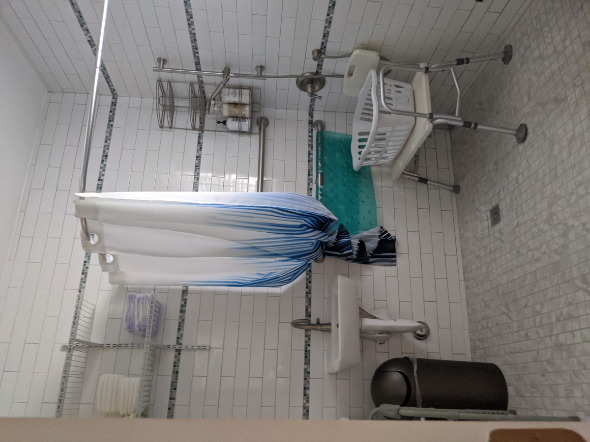 An accessible bathroom equipped with a shower chair, grab bars, and a shower curtain.