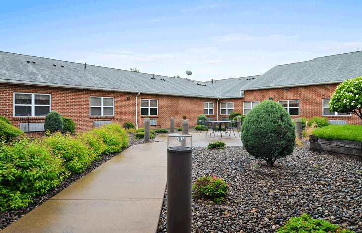 A landscaped courtyard with a pathway surrounded by shrubs and a brick building.
