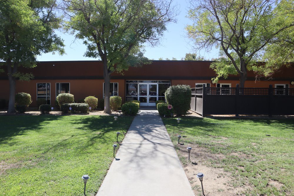 A building with a concrete pathway leading to its entrance, surrounded by trees and grass.