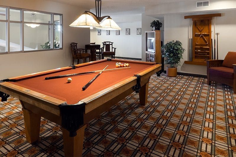 A cozy game room featuring a pool table with crossed cues, lit by elegant overhead lamps.