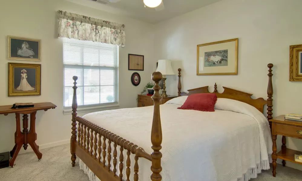 A cozy bedroom with a wooden bed, a window allowing natural light, and decorative elements.