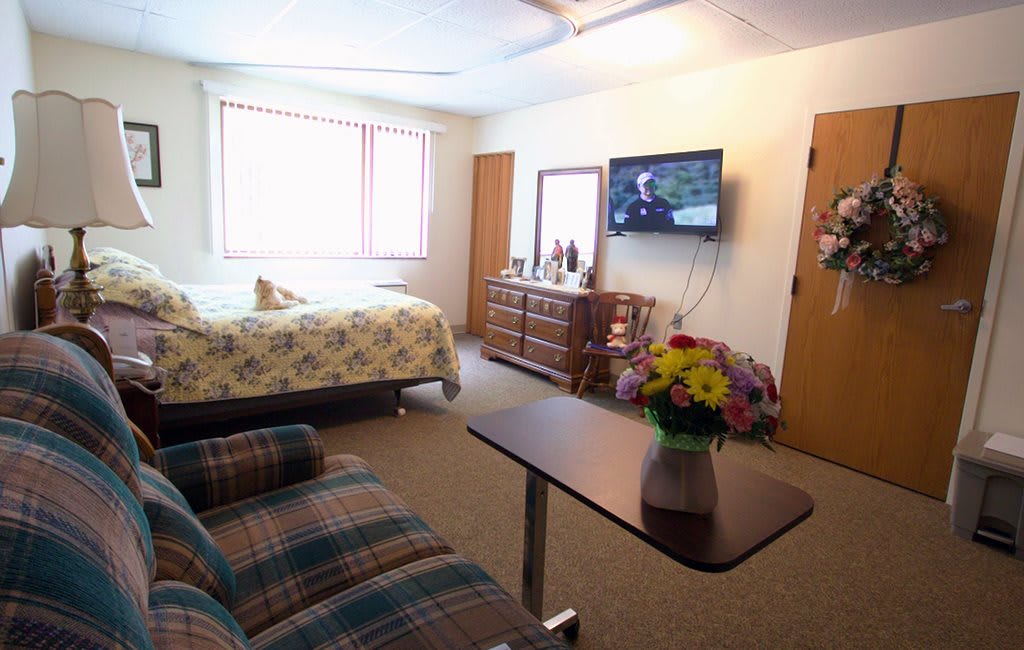 A cozy bedroom with a bed, TV, and a vase of flowers on the table.