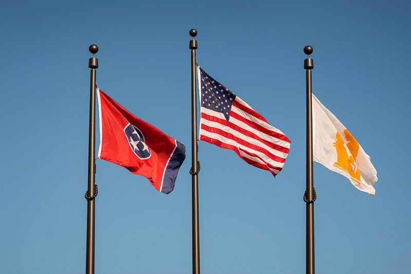 Three flags flying on flagpoles against a clear blue sky: Tennessee state flag, American flag, and an unidentified third flag.